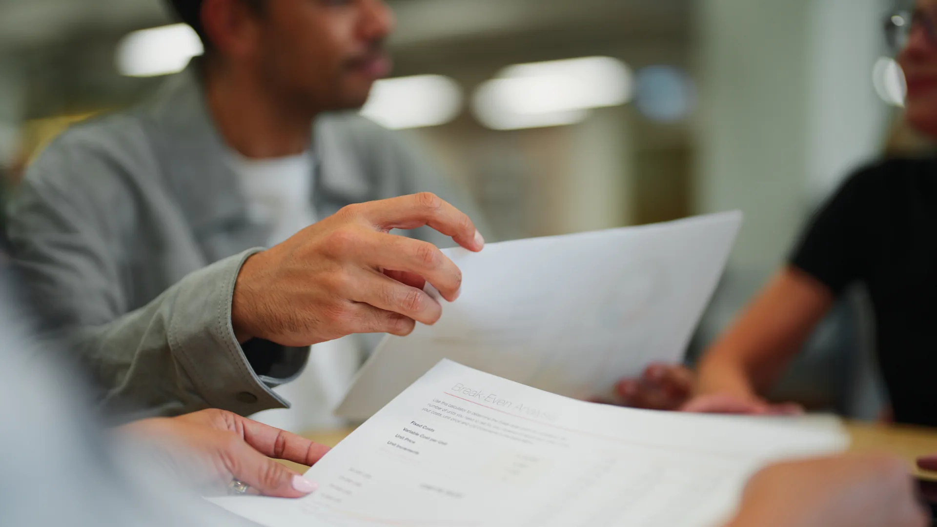 A person reading through a printed policy document across a table from someone else